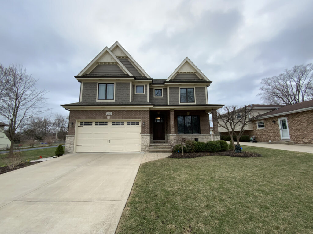 two-story-house-with-gray-siding-and-stone-accents-situated-on-a-landscaped-lawn-with-a-wide-driveway-and-cloudy-sky