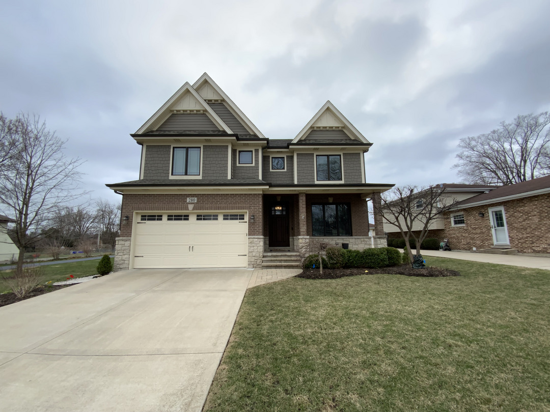two-story-house-with-gray-siding-and-stone-accents-situated-on-a-landscaped-lawn-with-a-wide-driveway-and-cloudy-sky